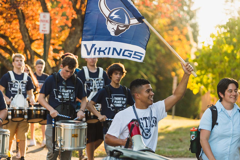 students marching, one holding a Western Viking flag and the others with drums