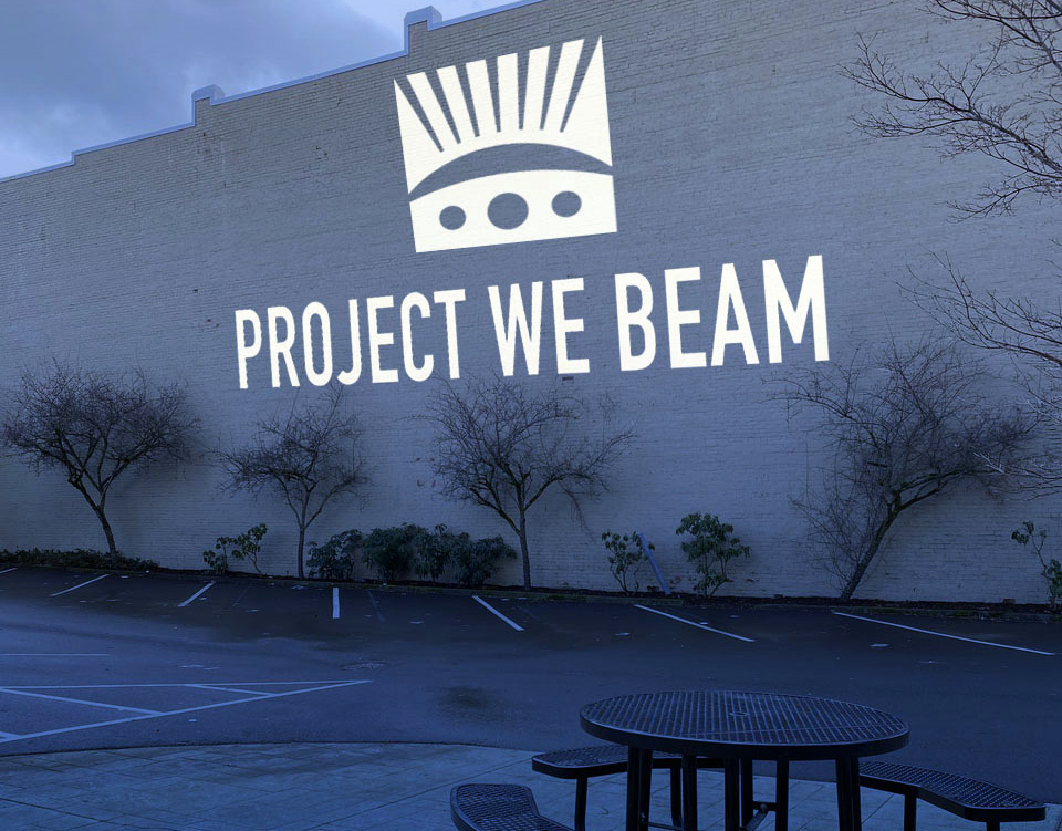 Project We Beam logo and text projected on the side of a building.