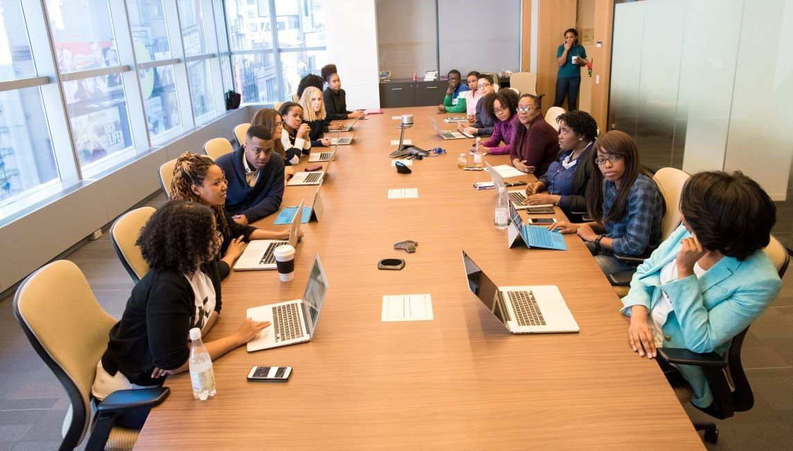 16 people sitting around a table working with laptops