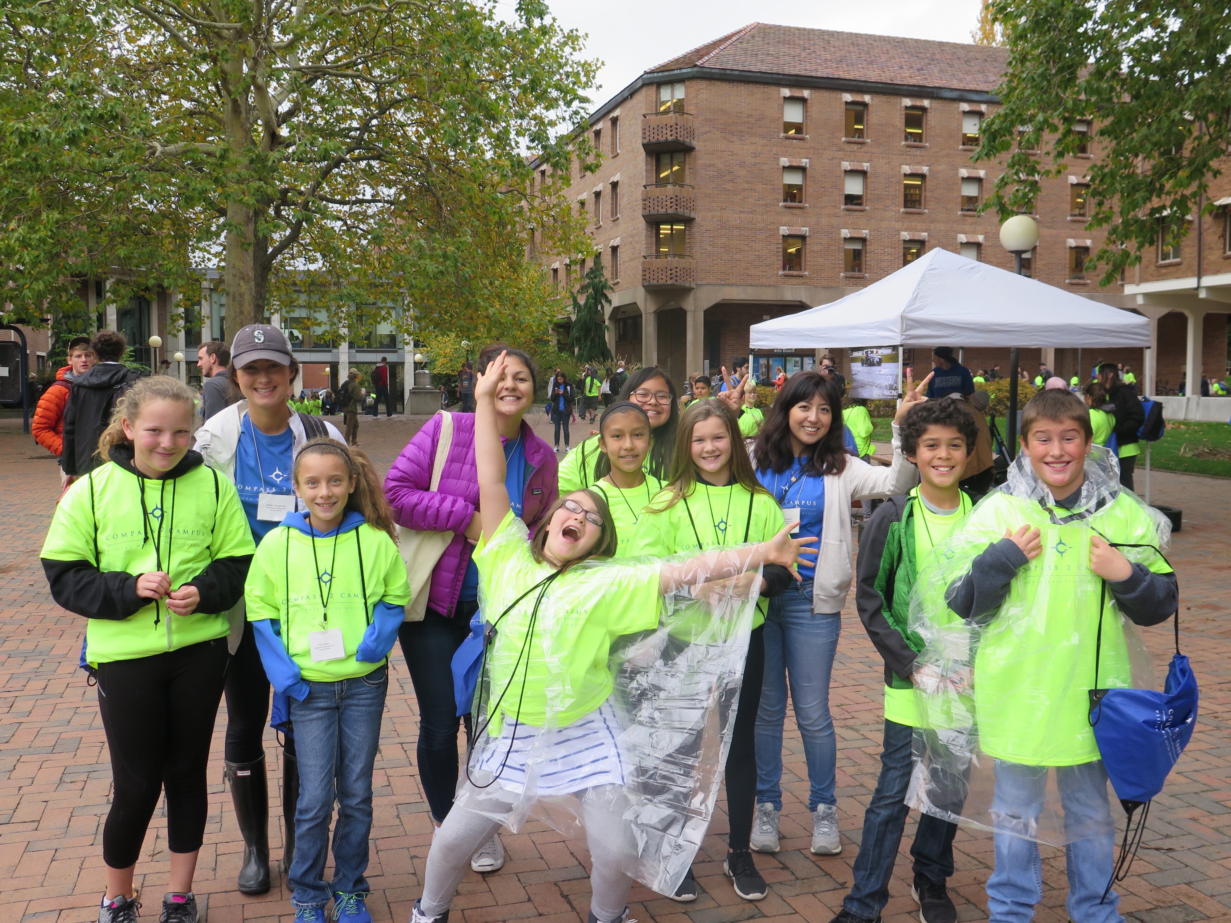A group of 5th grade students in lime green shirts, and college mentors smile and pose in Red Square during WWU Tour Day