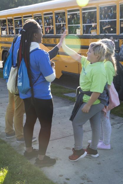 Two college mentors give high fives to two 5th grade students as they get on the bus after Tour Day.