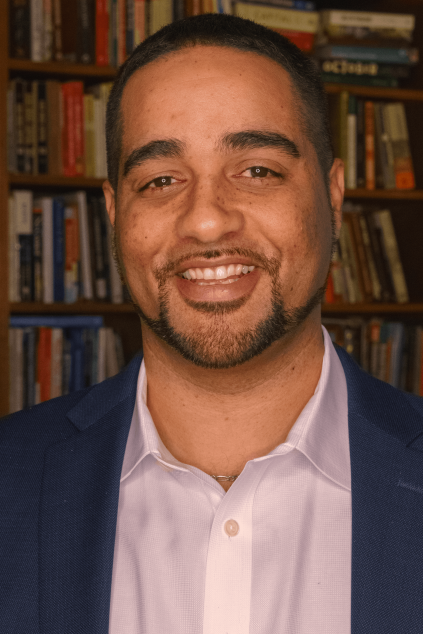 Jesse Hagopian smiling in a suit in front of a bookcase