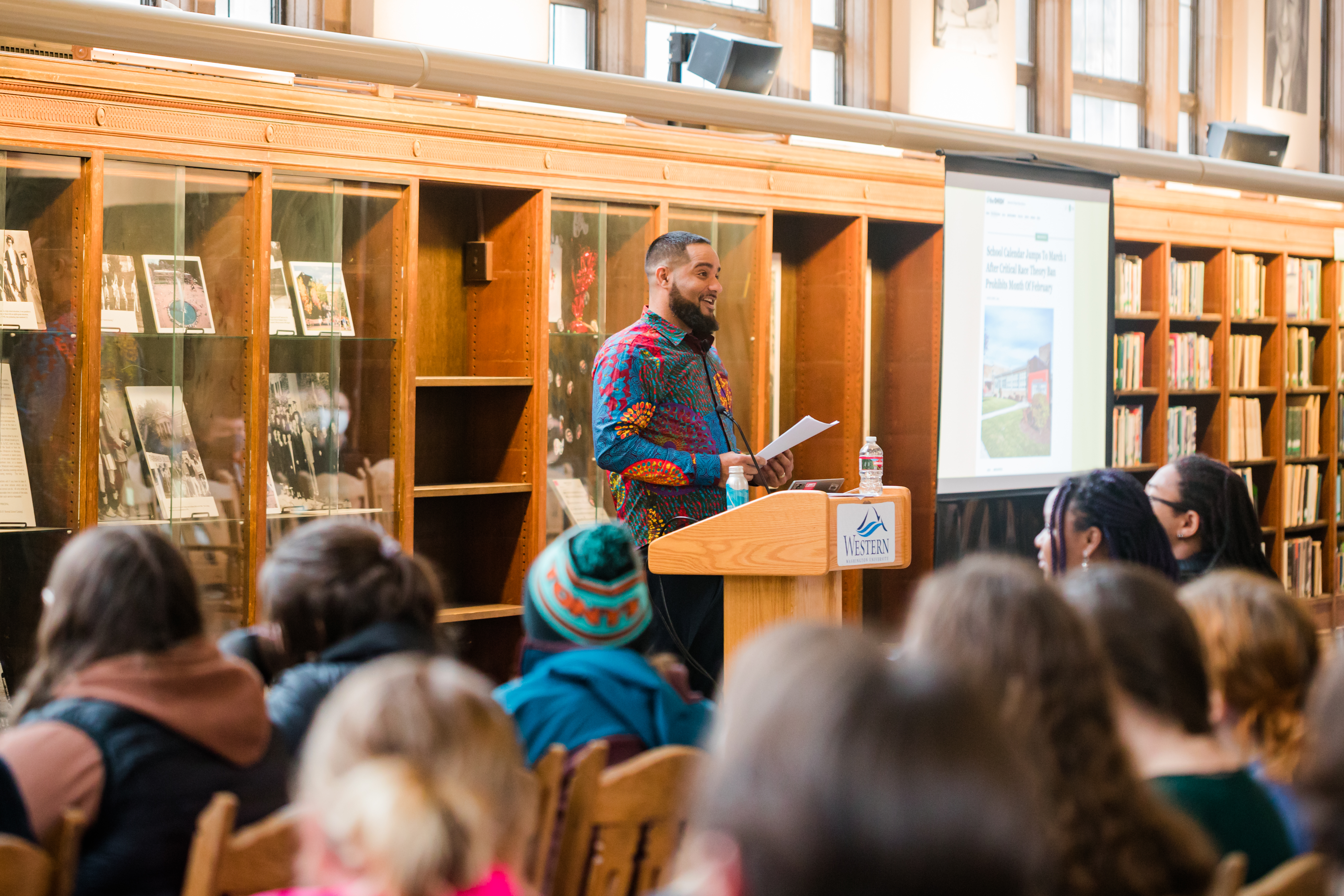 Jesse Hagopian stands at a podium in WWU's Wilson Library addressing a crowd of about 300.