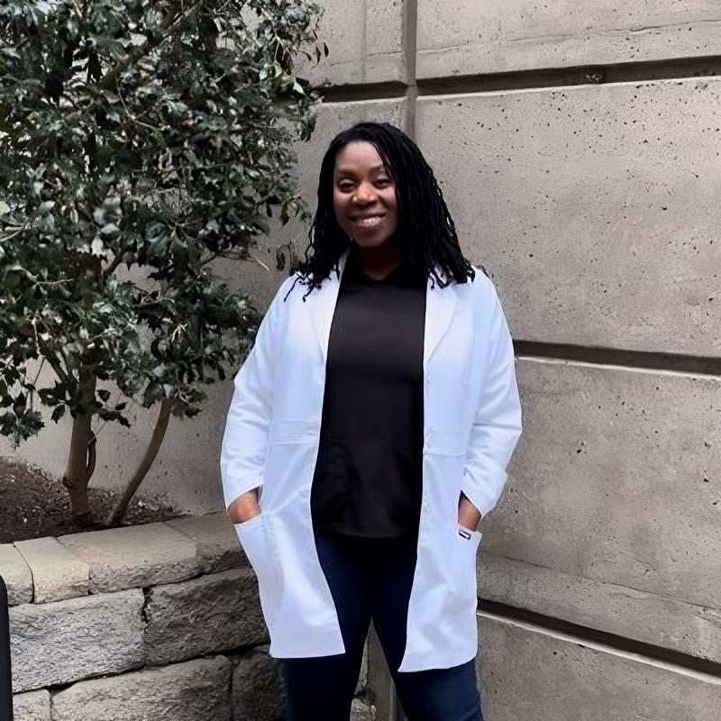 Devyn Nixon standing in front of concrete building with a white coat on smiling at the camera