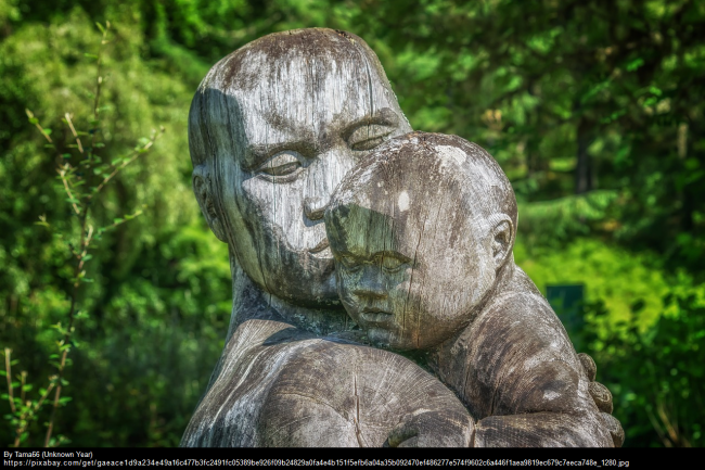 A rock sculpture of a parent holding a child in front of a green leafy background.