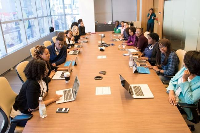 16 people sitting around a table working with laptops