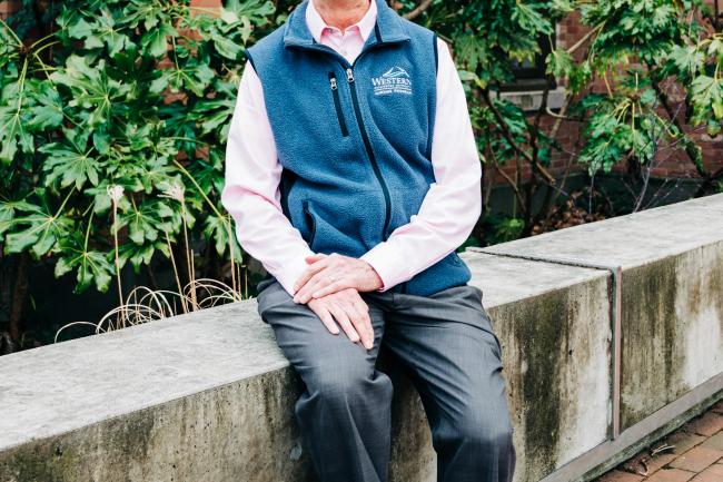 Bill Lonneman sitting on the concrete railing outside of Miller Hall in WWU Red Square