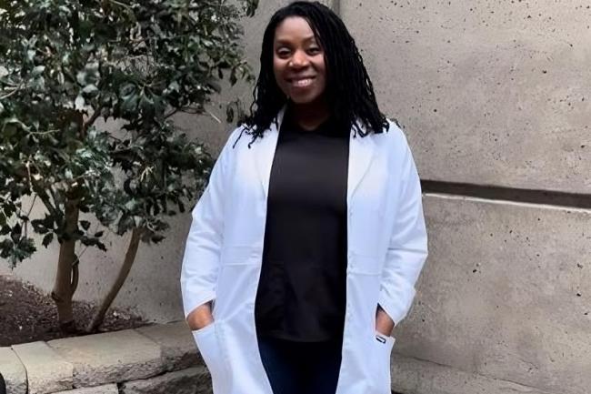 Devyn Nixon standing in front of concrete building with a white coat on smiling at the camera