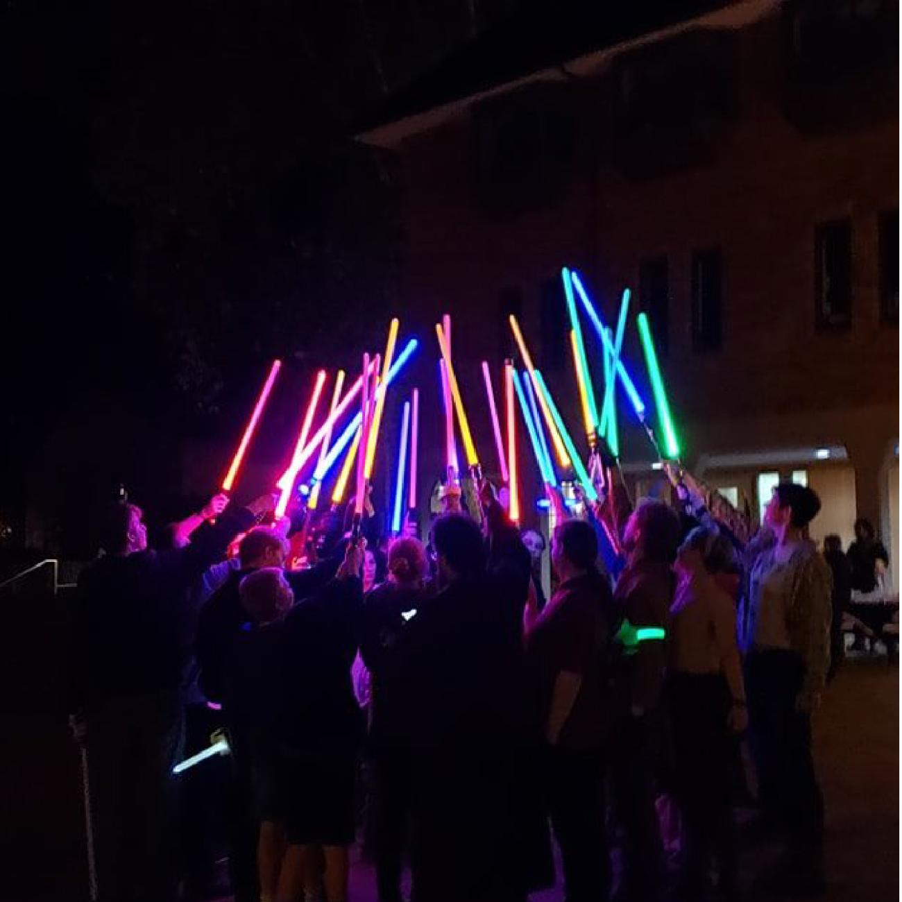 Students pointing lightsabers upwards outside in the dark for an Order of the Saber club meeting