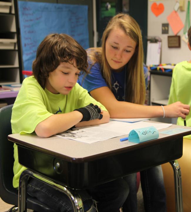 A college mentor and 5th grade student sit at a desk working on an assignment together.