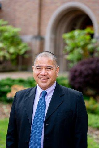 Kevin Roxas in a black blazer with a blue tie in front of old main