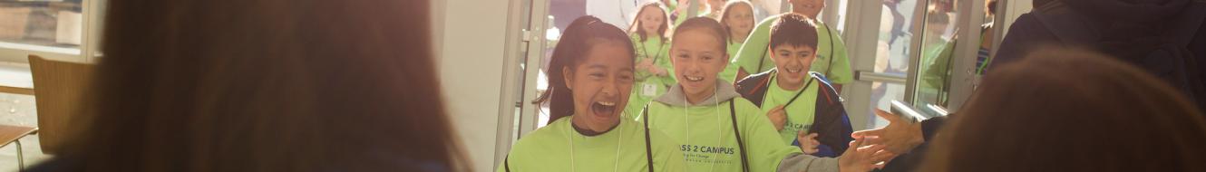 Smiling students in lime green "Compass to Campus" shirts walk through a door